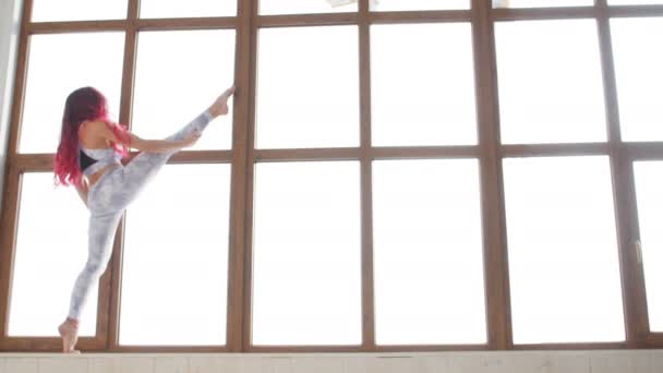 Konzept der Dehnung und Flexibilität. junge Frau in Sportkleidung beim Stretching am Fenster in einem weißen Interieur — Stockvideo