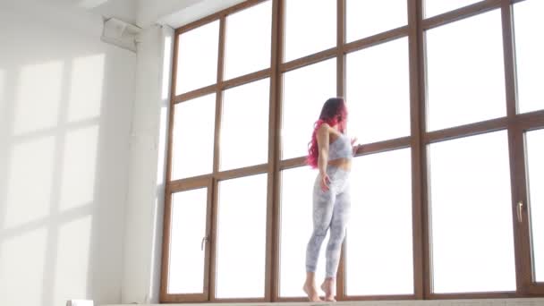 Concept of stretching and flexibility. Young woman in sportswear doing stretching near window in a white interior — Stock Video