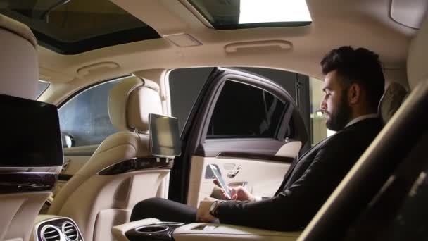 Молодой бизнесмен разговаривает по телефону в роскошной машине — стоковое видео