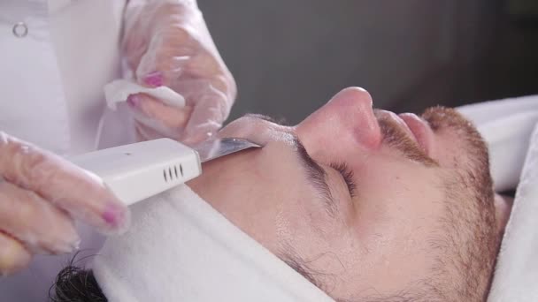 Nettoyeur à ultrasons pour le visage. Esthéticienne nettoie le visage d'un jeune homme — Video