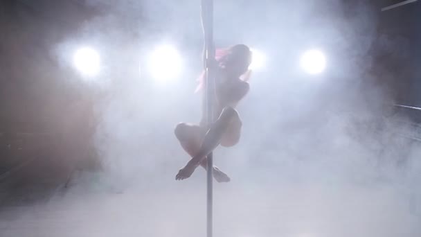 Молодая женщина на шесте танцует в темной комнате с подсветкой и дымом — стоковое видео