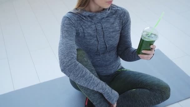 Sport and healthy lifestyle concept. Young woman with cup of smoothie at yoga studio or gym — Stock Video
