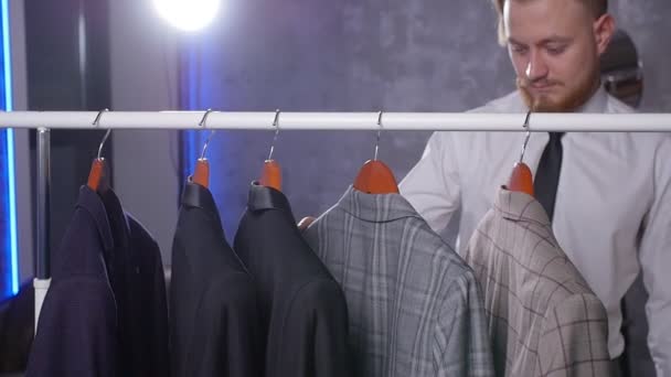 Молодий елегантний чоловік вибирає класичний костюм в магазині — стокове відео
