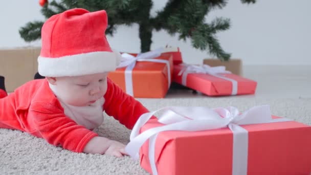 Kerst concept. Schattige baby in het kostuum van de Kerstman, op zoek naar een geschenk — Stockvideo