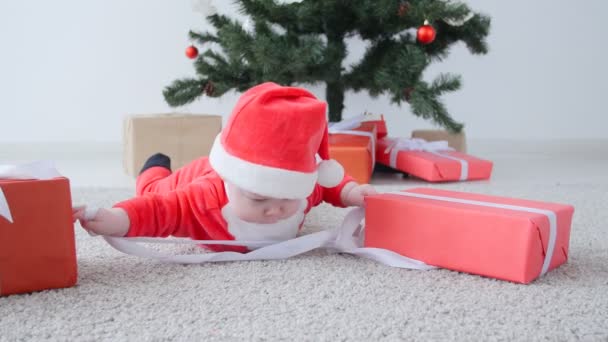 Χριστουγεννιάτικη ιδέα. Χαριτωμένο μωρό στο κοστούμι του Άγιου Βασίλη, ψάχνει ένα δώρο — Αρχείο Βίντεο