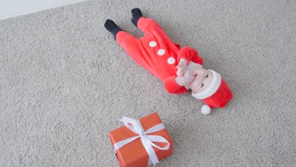 Weihnachtskonzept. niedliches Baby im Kostüm von Weihnachtsmann, suchen ein Geschenk — Stockvideo