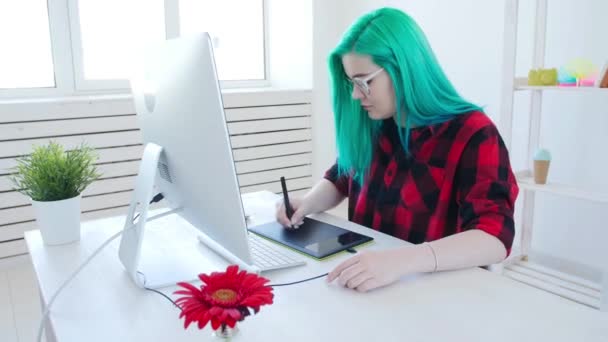 Молодой графический дизайнер с цветными волосами работает на компьютере с помощью планшета — стоковое видео