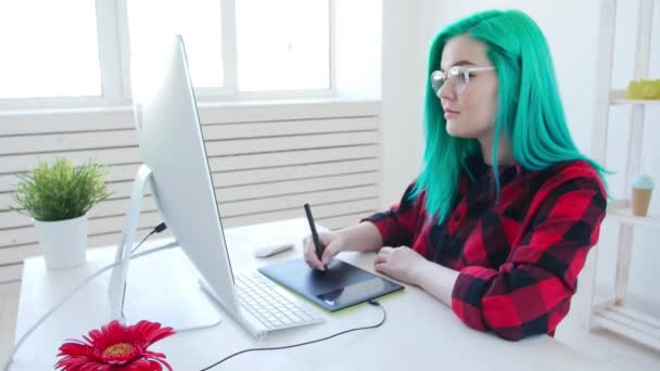 Młody projektant graficzny z kolorową fryzurą pracując na komputerze za pomocą tabletu — Wideo stockowe