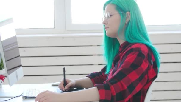 Молодой графический дизайнер с цветными волосами работает на компьютере с помощью планшета — стоковое видео