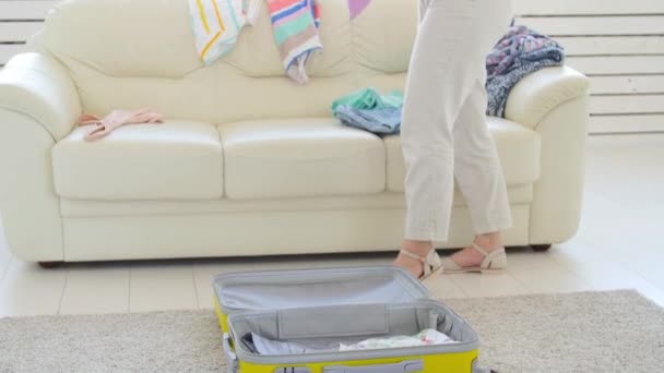 Travel and vacation concept. Happy young woman is packing colorful summer clothes into luggage suitcase for a new journey — Stock Video