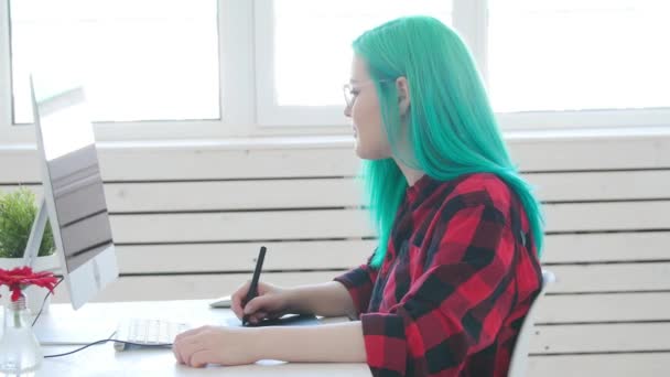 Concepto de trabajo autónomo o de oficina. Joven diseñadora gráfica femenina con cabello coloreado trabajando en la oficina o en casa — Vídeos de Stock