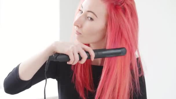 Haar- und Friseurkonzept. junge Frau mit roten Haaren kreiert eine Frisur mit Bügeleisen oder Zange — Stockvideo