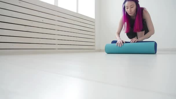 Concepto de deporte y salud y relajación. Mujer joven con una esterilla de yoga y ejercicios en un apartamento o gimnasio — Vídeos de Stock