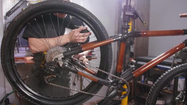Концепция обслуживания велосипедов. Молодой человек ремонтирует и обслуживает велосипед в мастерской — стоковое видео