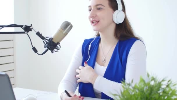 Concepto de streaming y radiodifusión. Mujer joven con auriculares y hablando en la estación de radio en línea — Vídeo de stock