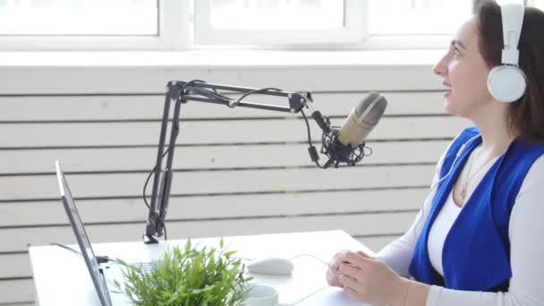 Concepto de streaming y radiodifusión. Mujer joven con auriculares y hablando en la estación de radio en línea — Vídeos de Stock