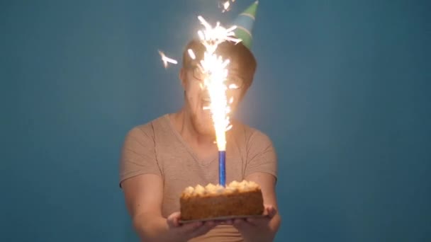 Concepto de celebración y diversión. Sonriendo joven loco feliz en sombrero de fiesta sosteniendo un pastel de cumpleaños — Vídeos de Stock