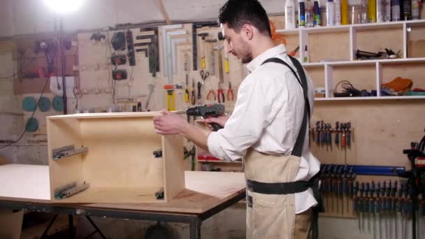Концепция бизнеса и производства. Молодой человек в мастерской собирает мебель — стоковое видео