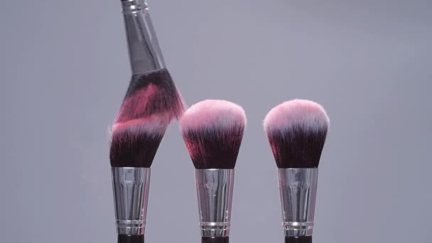 Cepillo de maquillaje con salpicaduras de polvo rosa explosión sobre fondo gris en cámara lenta — Vídeo de stock