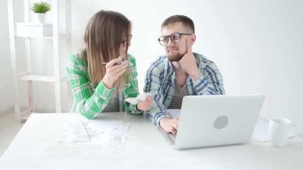 El esposo y la esposa cuentan las compras y facturas del mes pasado y registran los resultados en su contabilidad doméstica en un cuaderno y en una computadora portátil. Concepto de ahorro y contabilidad — Vídeos de Stock
