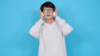 Müzik konseptine olan sevgi. Olgun Kadın, mavi arka planda Kulaklıkla Müzik Aktarıyor