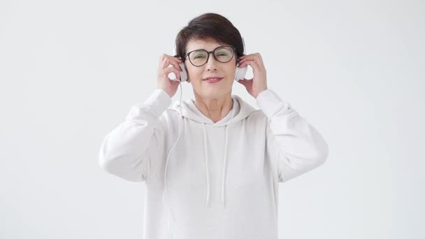 Liefde voor muziek concept. Rijpe vrouw streamt muziek in een koptelefoon op een witte achtergrond — Stockvideo