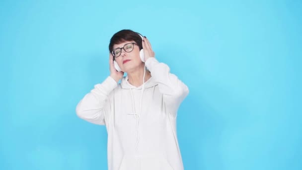 Amor por el concepto musical. Mujer madura transmite música en auriculares sobre un fondo azul — Vídeos de Stock