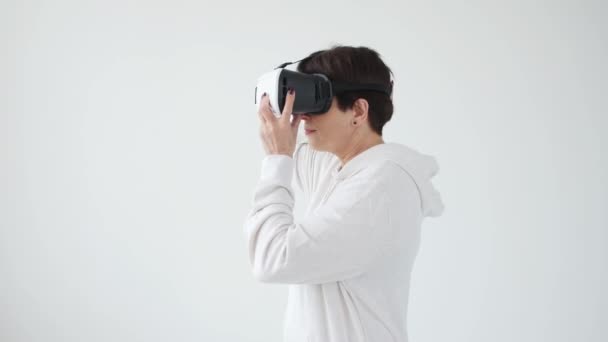 Mulher de meia-idade em uma camisola branca assistindo a um filme com óculos de realidade virtual. O conceito de futurismo e novas tecnologias . — Vídeo de Stock