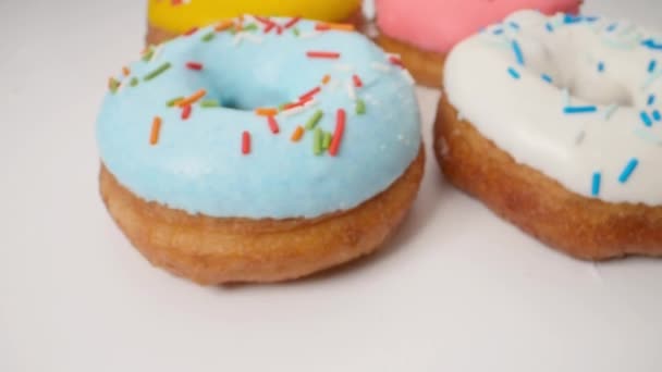 Вкусные разноцветные пончики на белом фоне. Гладкое движение тележки — стоковое видео