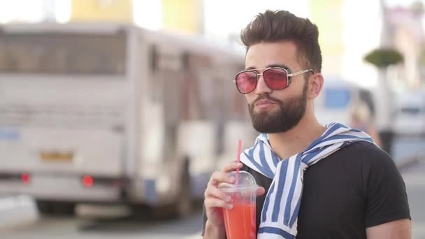 Концепция уличной еды и городской жизни. Молодой улыбающийся бородатый мужчина держит чашку с коктейлем или лимонадом — стоковое видео