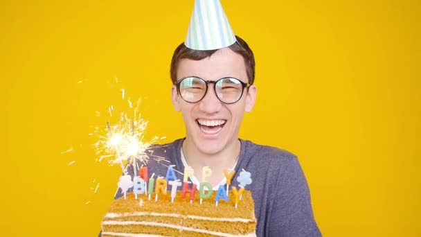 Gelukkige verjaardag concept. Jonge grappige man met een cake o een oranje achtergrond — Stockvideo