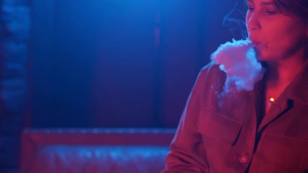 Junge Frau raucht Vaporizer in Club in buntem Licht — Stockvideo