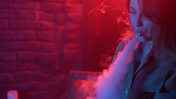 Νεαρή γυναίκα κάπνισμα ψεκαστήρα στο Club σε ένα πολύχρωμο φως — Αρχείο Βίντεο