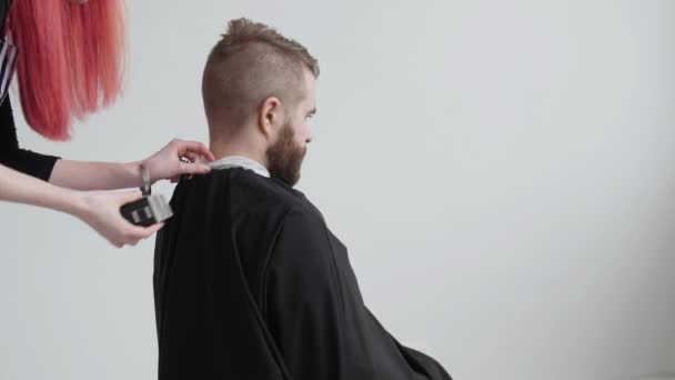 Jeune coiffeuse rousse coupe les cheveux d'un homme barbu client — Video