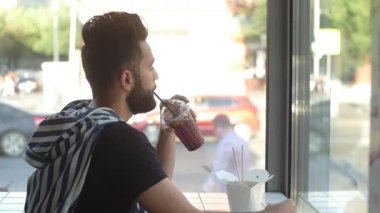Bir kafede meyve suyu smoothie içme genç adam, kentsel şehir arka plan