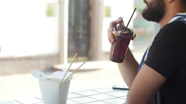 Giovane uomo che beve frullato di succo in un caffè, sfondo urbano della città — Video Stock