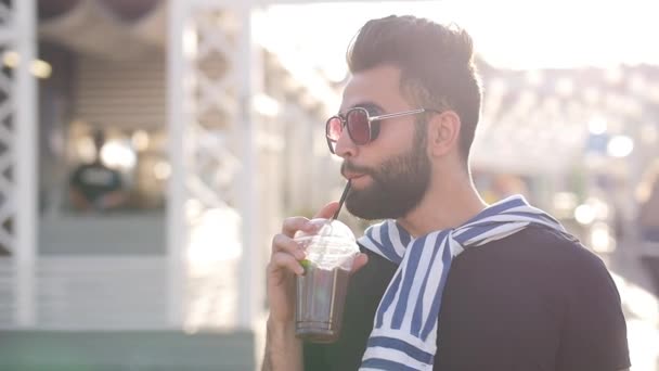 Mladý muž pije šťávu v kavárně, zázemí městského města — Stock video