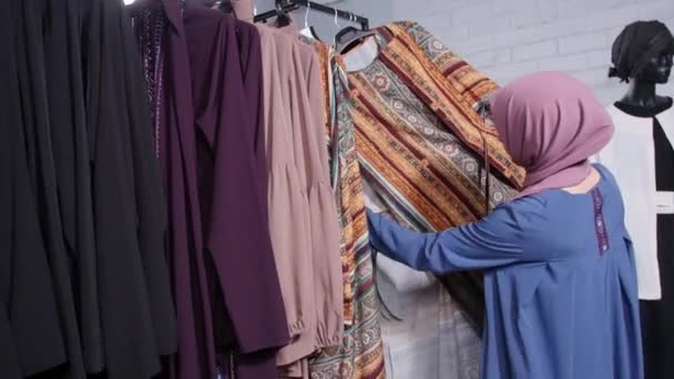 Koncepció a vásárlás muzulmán országokban. Egy fiatal muszlim nő választotta ruhát a boltban — Stock videók