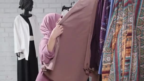 Concept of shopping in Muslim countries. A young Muslim woman choosing clothes at the store — Stock Video