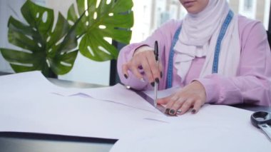 Küçük işletme ve hobi konsepti. Müslüman kadın moda tasarımcısı terzi dükkanında masada kağıt desen sabitleme