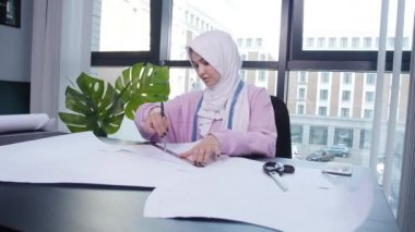 Küçük işletme ve hobi konsepti. Müslüman kadın moda tasarımcısı terzi dükkanında masada kağıt desen sabitleme