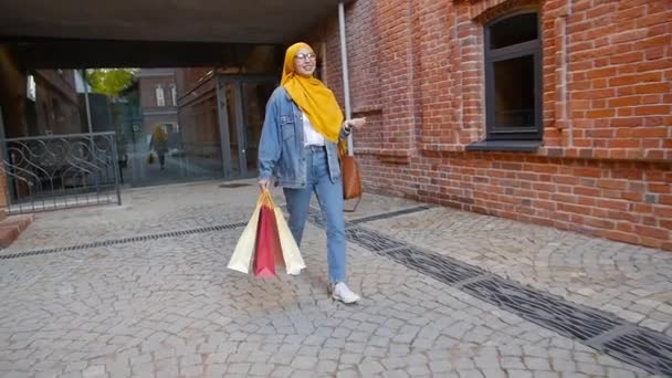 Shopping concept. Stylish muslim girl is walking along the city street with shopping — Stock Video