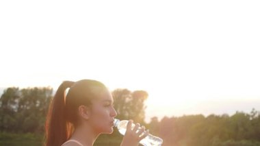 Spor ve fitness konsepti. Güzel genç sportif kadın egzersiz sonrası bir günbatımı önünde içme