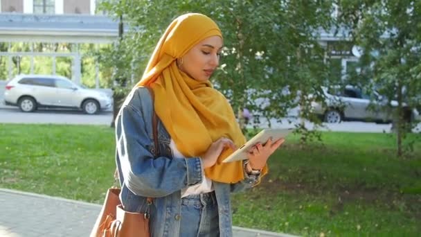 Jeune femme musulmane dans le sourire foulard tête avec tablette mobile à l'extérieur — Video