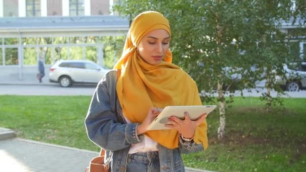 Mujer musulmana joven en la cabeza bufanda sonrisa con tableta móvil al aire libre — Vídeos de Stock