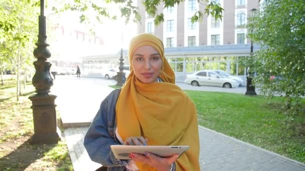 Jeune femme musulmane dans le sourire foulard tête avec tablette mobile à l'extérieur — Video