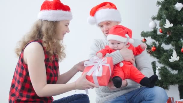 Vacaciones familiares y concepto de Navidad. Joven madre y padre con un niño desempaquetar un regalo de Navidad — Vídeos de Stock