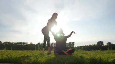 Gün batımında açık havada germe egzersizi yaparken neşeli eğitmen ve pozitif kadın ışınlama