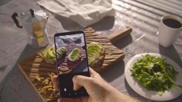 健康饮食的概念。手拿着鳄梨和智能手机拍照三明治 — 图库视频影像