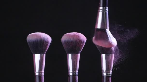 Il concetto di bellezza. Pennelli cosmetici con polvere cosmetica rosa che si diffonde su fondo nero al rallentatore — Video Stock